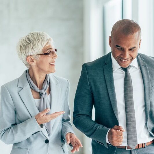 Two smiling business people walking through office hall and talking